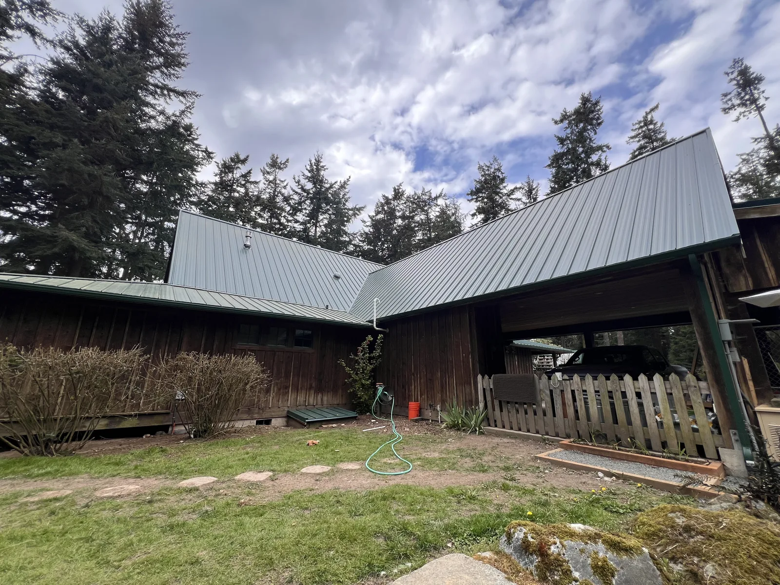 Dark brown house and carport with a new grey metal roof behind a picket fence