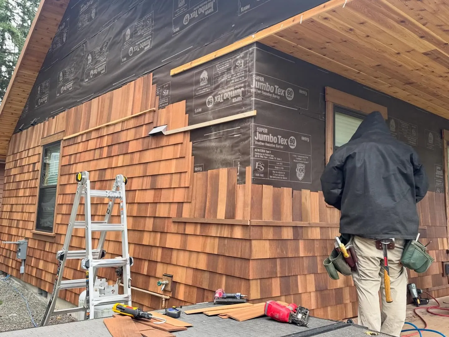 Cedar shingle siding going on over building paper, with an installer at the wall