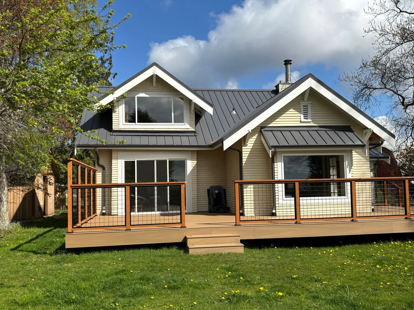 Cream house with a dark standing-seam metal roof and a deck with cable railing