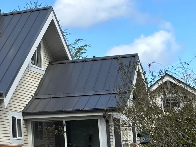 Side of a cream lap-sided house with a dark metal roof and a deck