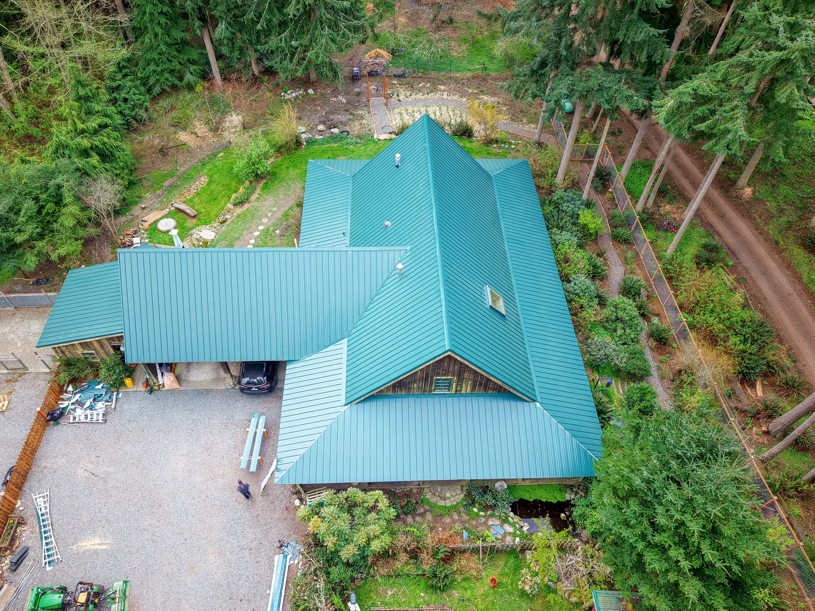 Drone view of a home with a new green standing-seam metal roof, with its hips, valleys and skylight