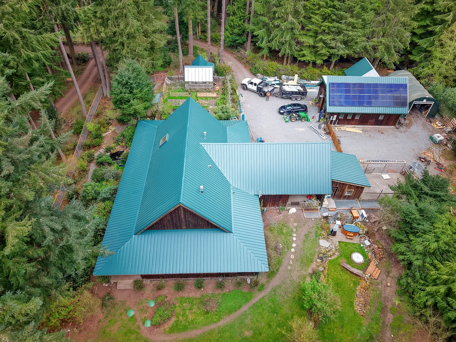 Drone view of a home and a barn with new green metal roofs, the barn roof carrying solar panels