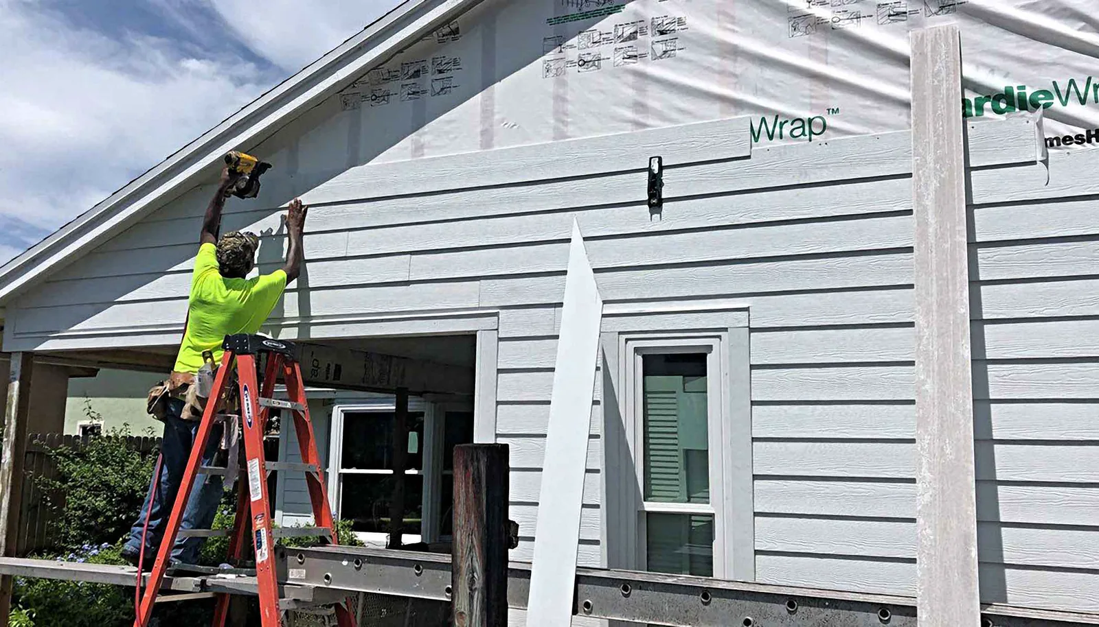 Installer nailing new fiber cement lap siding onto a house wall over house wrap