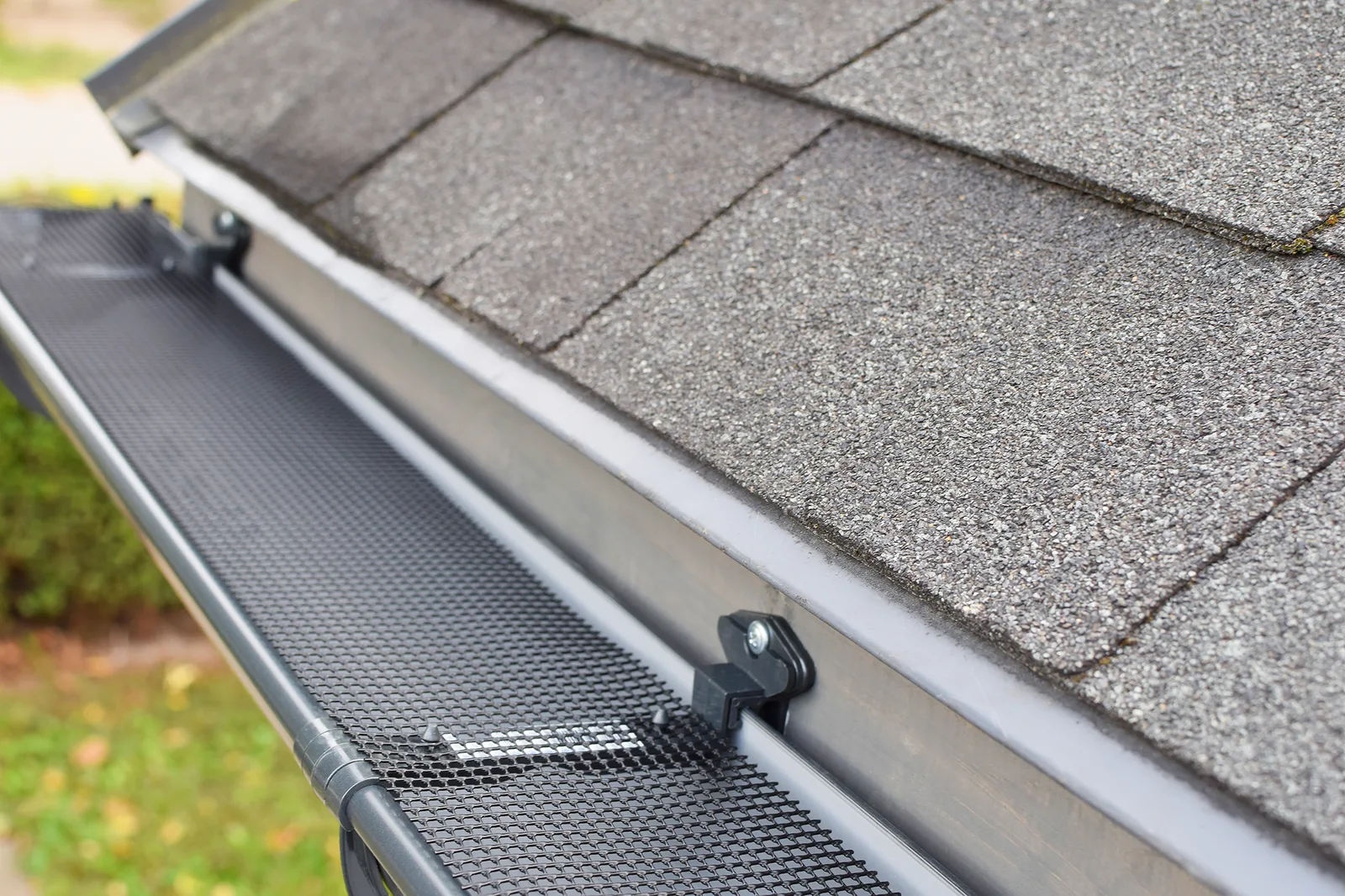 Gutter guard clipped onto a gutter along a shingle roof edge