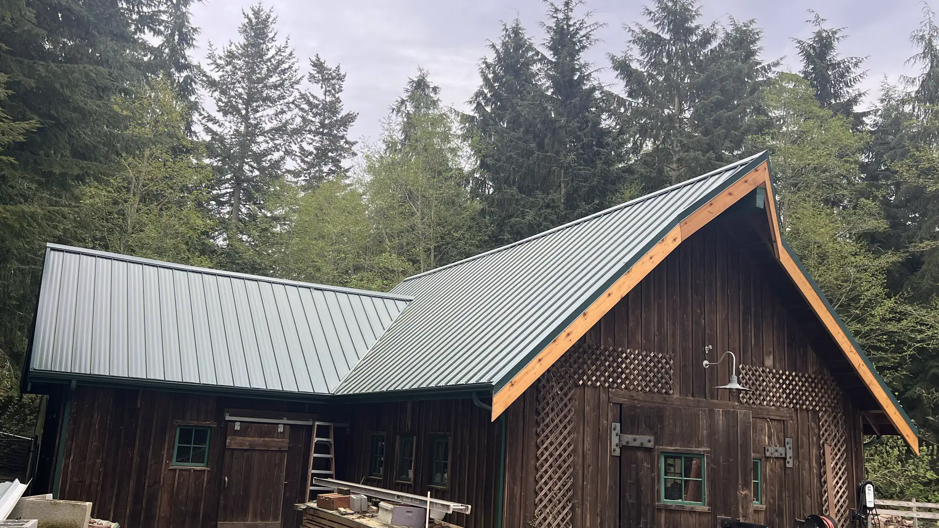 New dark green standing-seam metal roof on a cedar-sided barn surrounded by fir trees on Whidbey Island