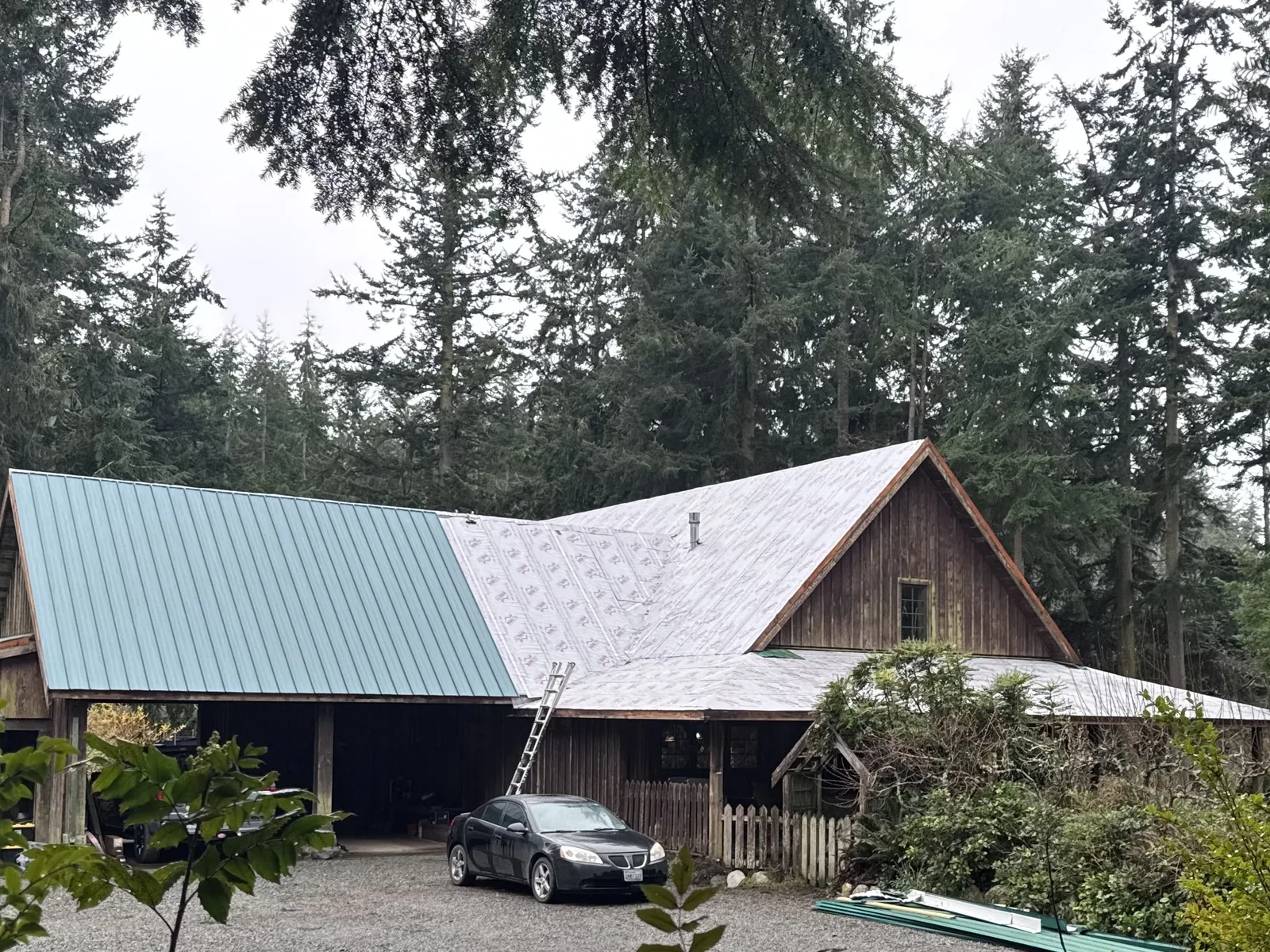 House roof covered in underlayment beside a green metal carport roof during a re-roof