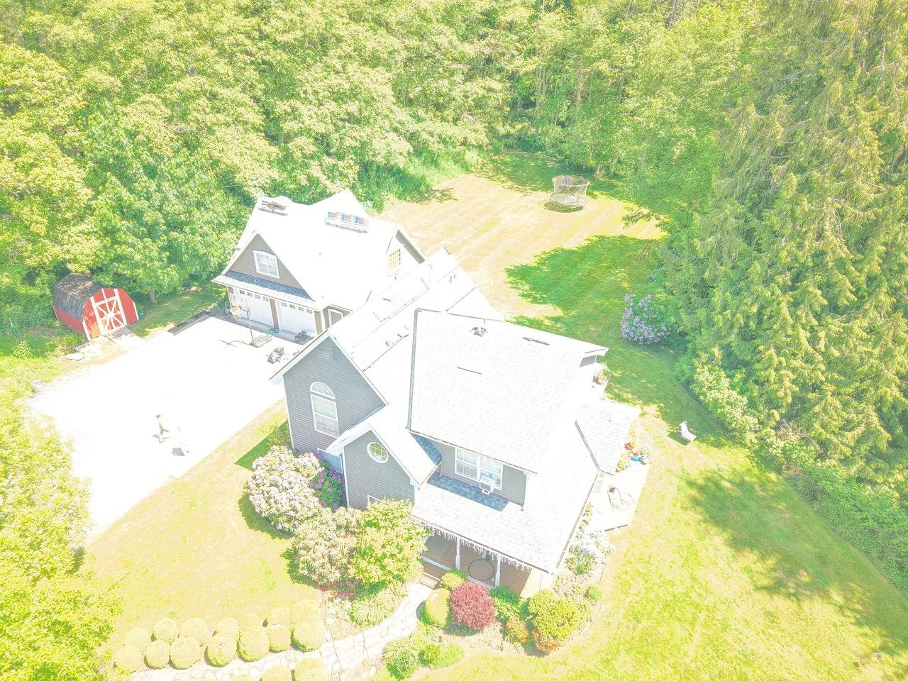 Drone view of a large grey-sided home with a light grey shingle roof among trees