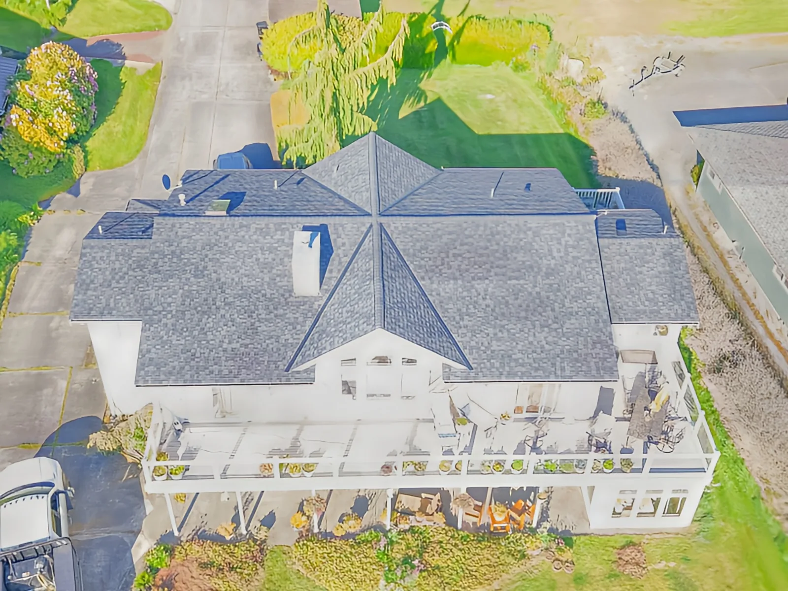 Drone view of a large white home with a grey shingle roof and a wraparound deck
