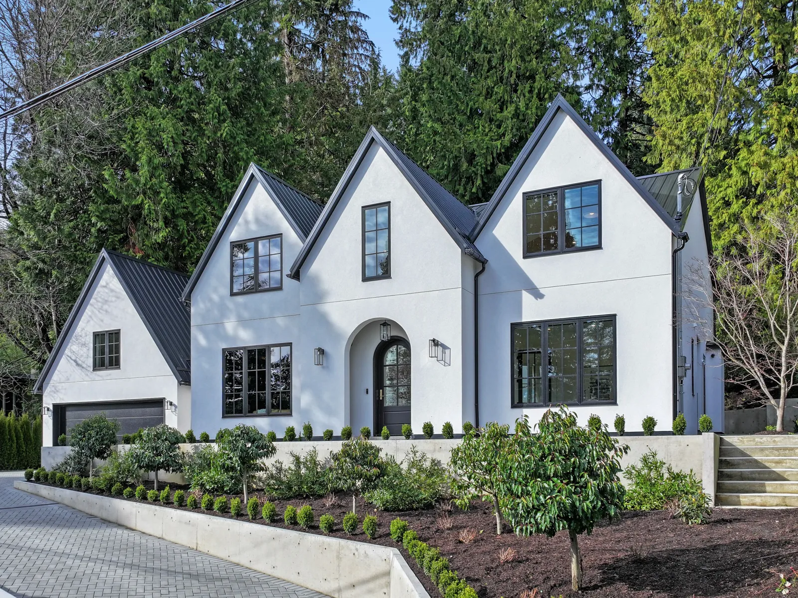 Home with new black-framed windows and fir trees behind