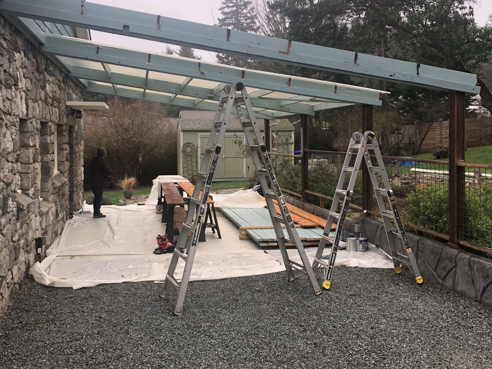 New patio cover frame along a stone wall with ladders set up under it