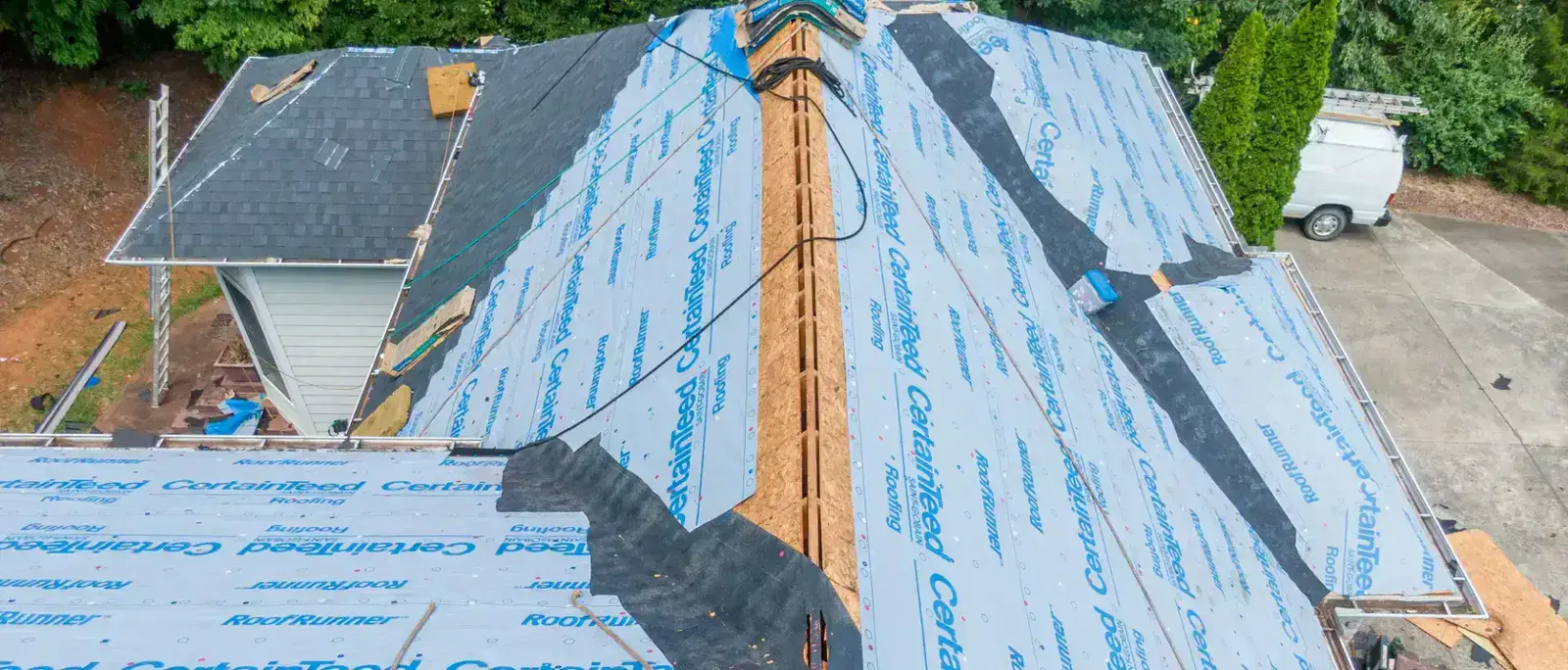 Roof mid-replacement seen from above, with synthetic underlayment down and the old shingles torn off