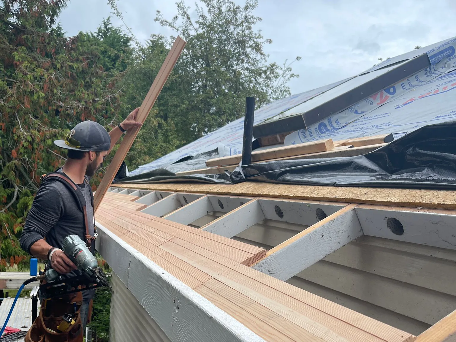 Roofer on scaffolding beside new rafter blocking and roof decking during a tear-off