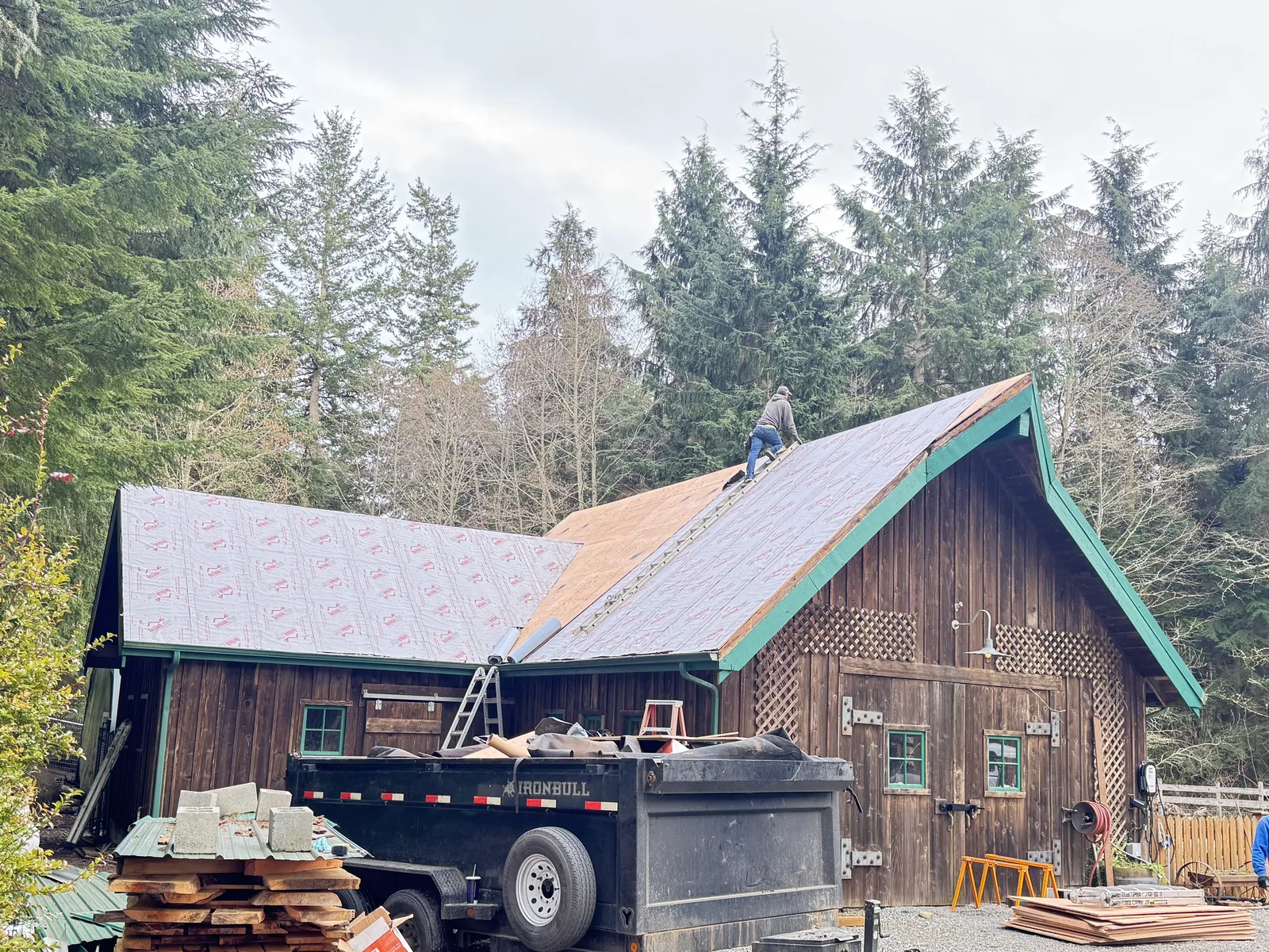 Roofer laying underlayment over new plywood decking on a cedar barn
