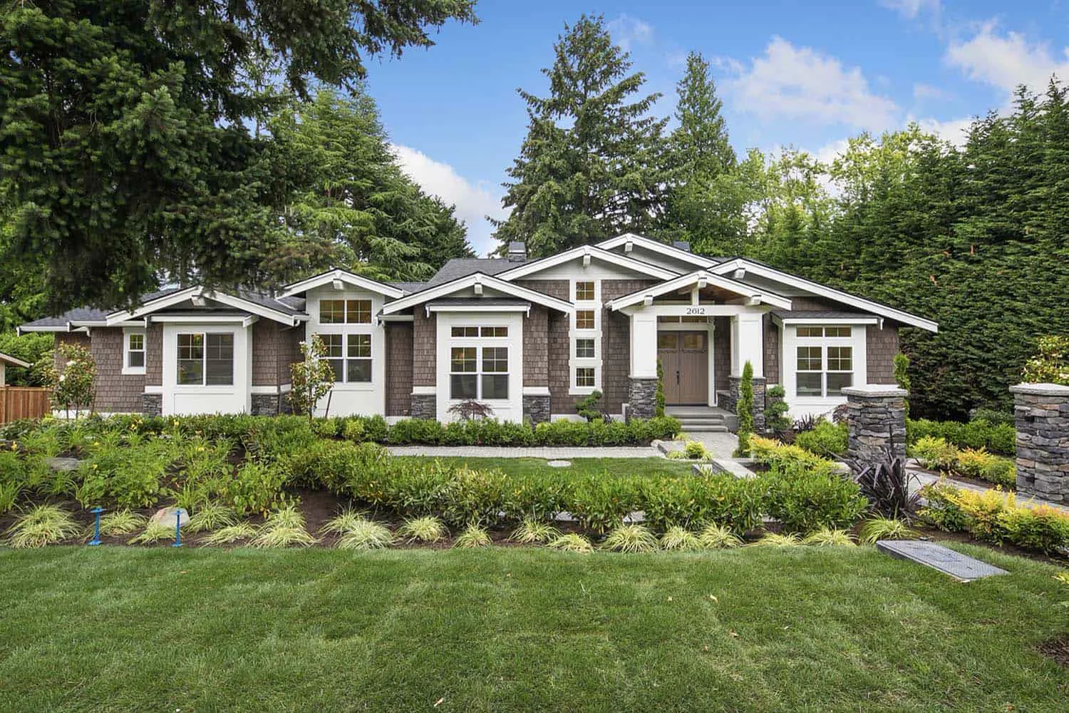 Brown shingle-sided home with a grey roof and tall fir trees behind it