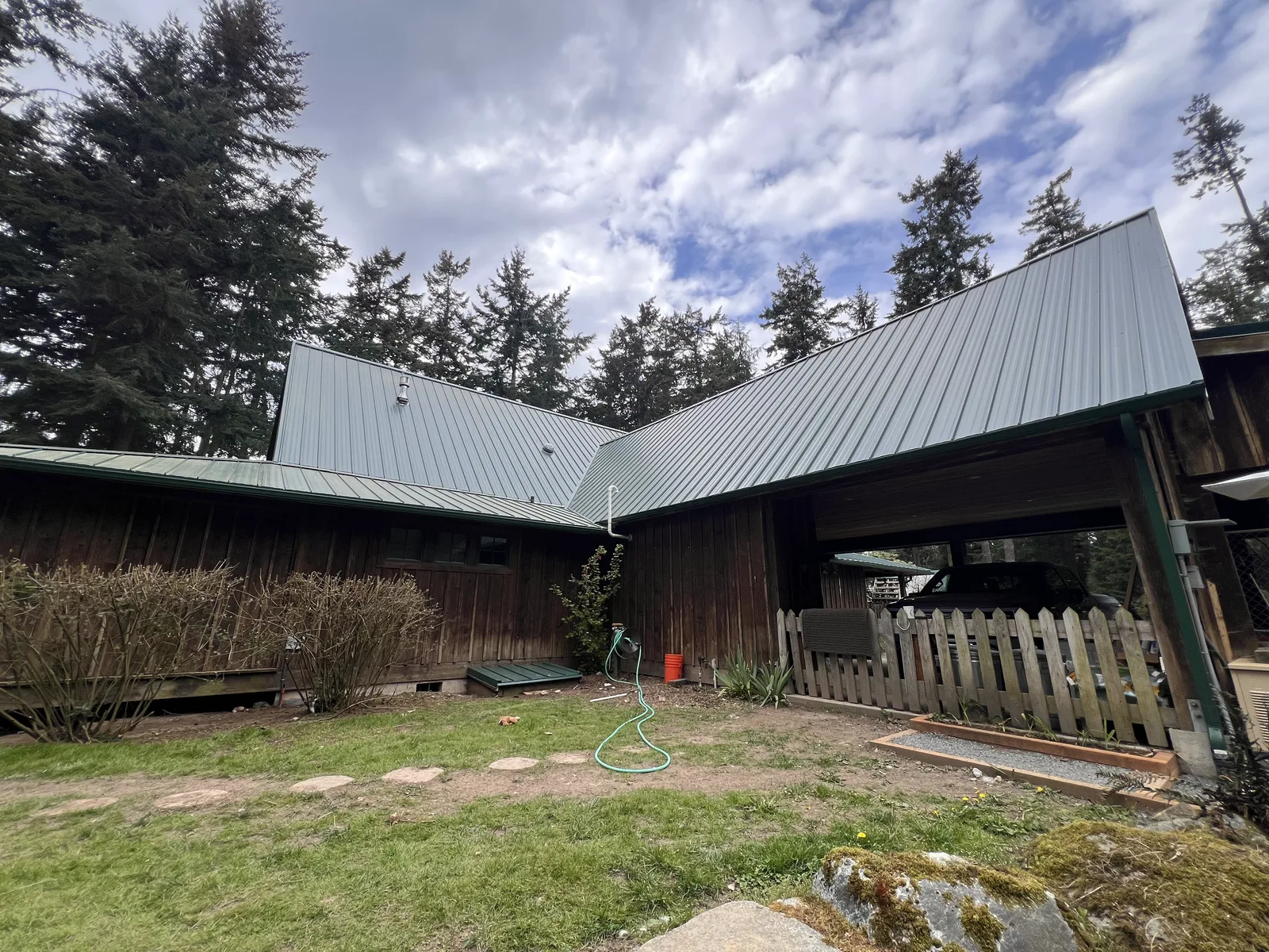 Dark brown house with a new grey-green standing-seam metal roof under a cloudy sky