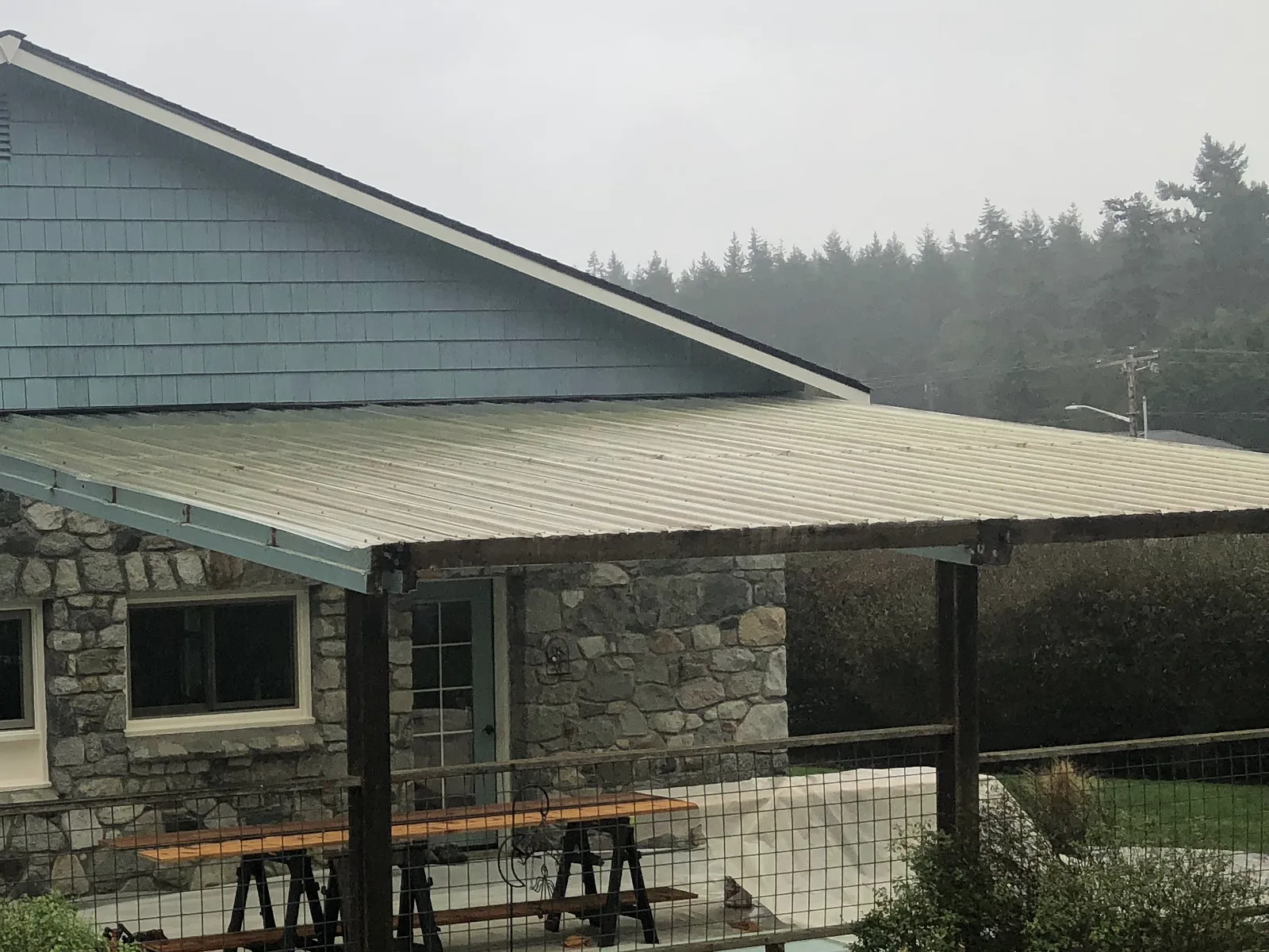 New metal roof panels over a stone home's covered patio on a foggy morning