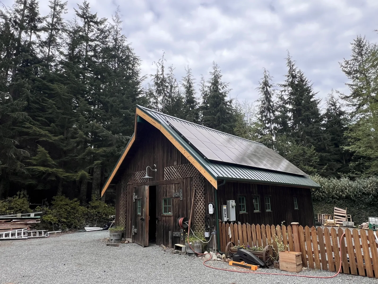 Cedar barn with a standing-seam metal roof and rooftop solar panels among fir trees