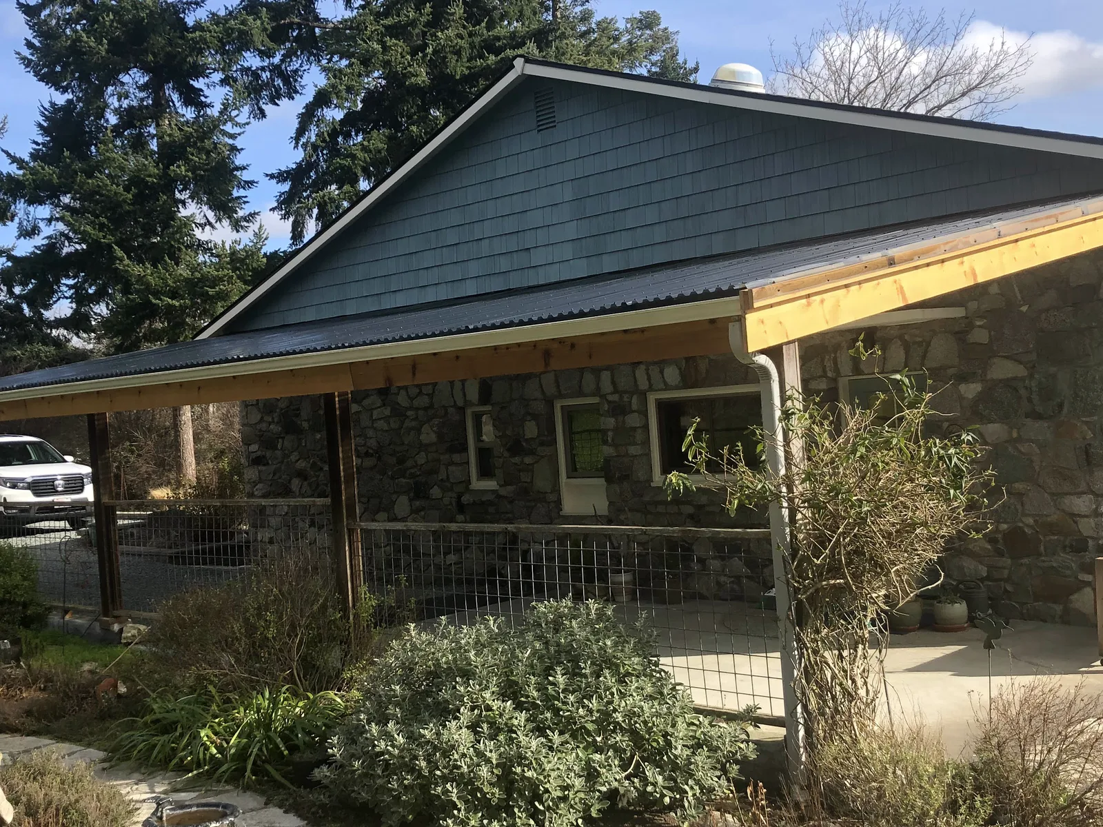 New metal porch roof and cedar beams on a stone-faced home with a shingled gable