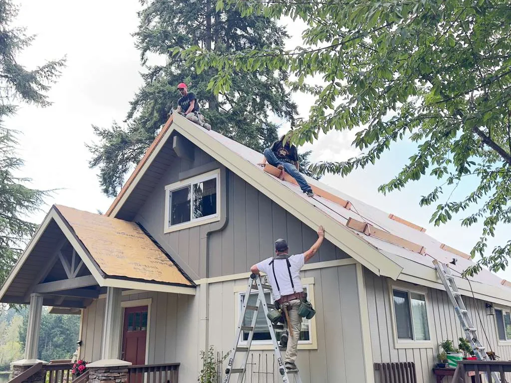 Roofing crew working on a cottage roof, one on the ridge and one on a ladder at the eave