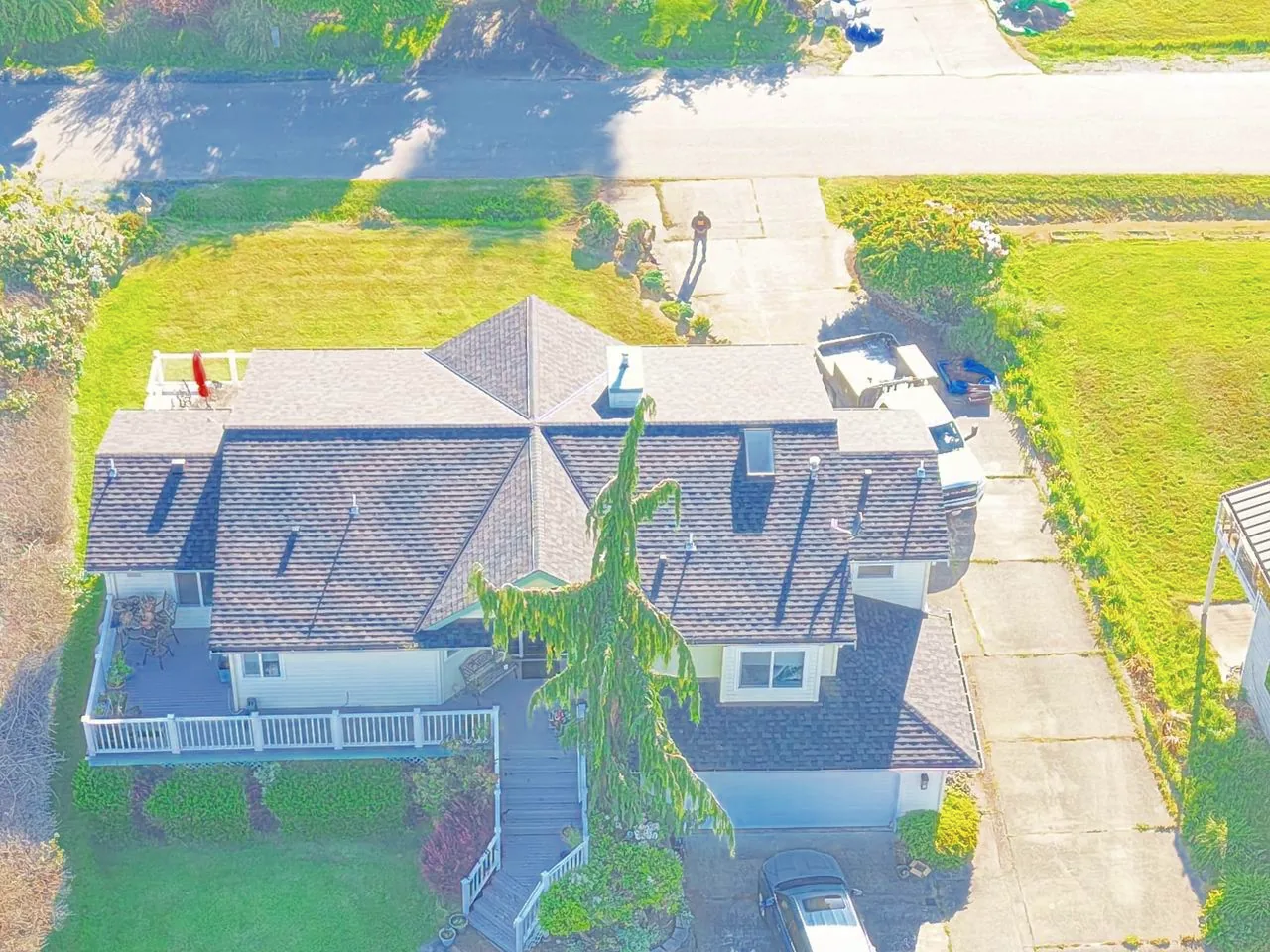 Drone view of a large home with a grey shingle roof, a deck and a front stair