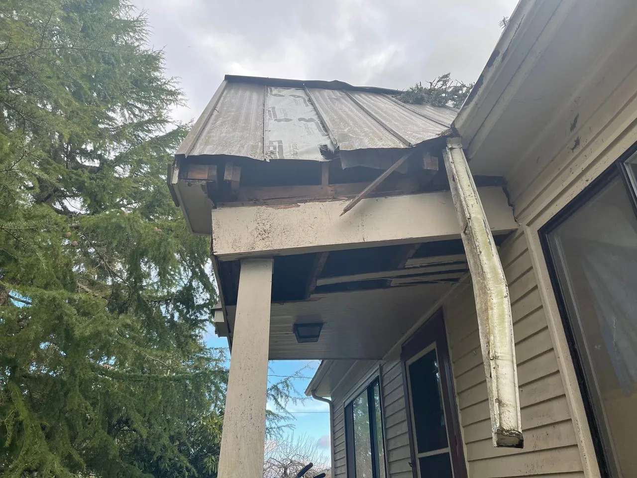 Storm-damaged porch roof with a broken gutter hanging off the eave