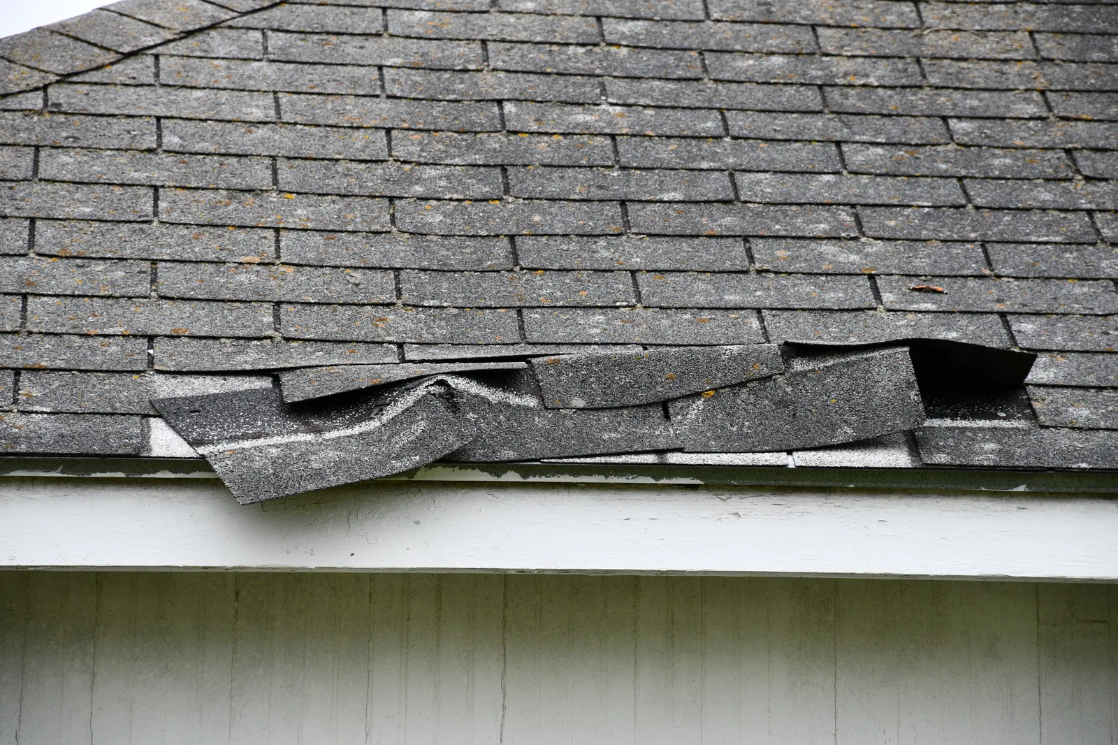 Curling and lifted shingles along the edge of a weathered roof after wind damage
