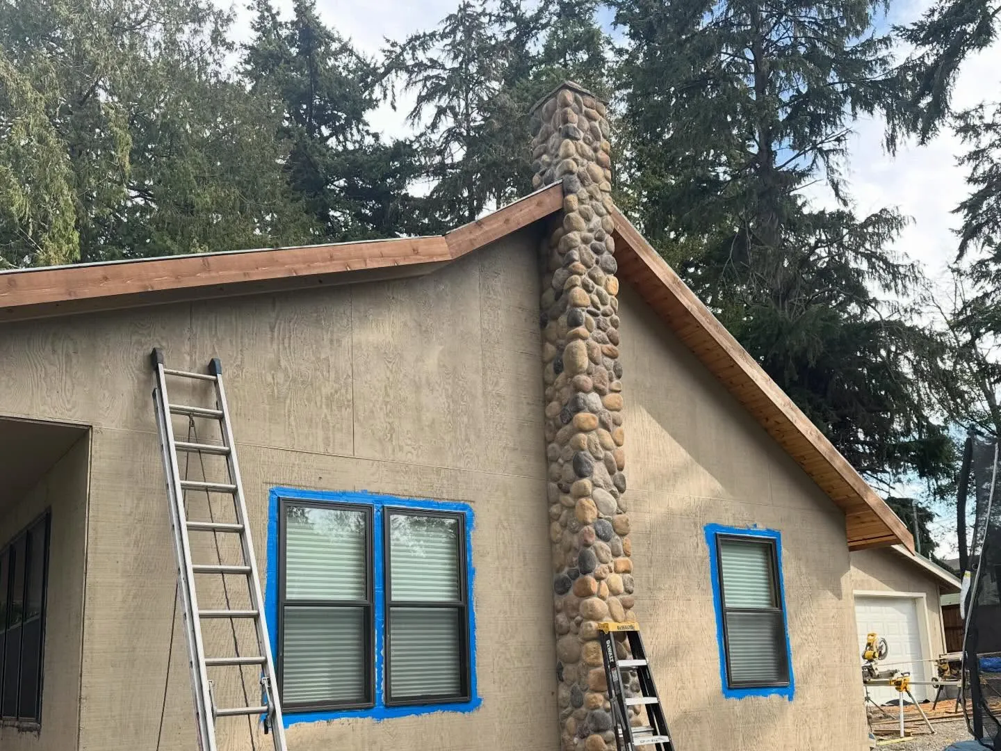 Stucco house with taped windows and a river rock chimney before its cedar shingle re-side