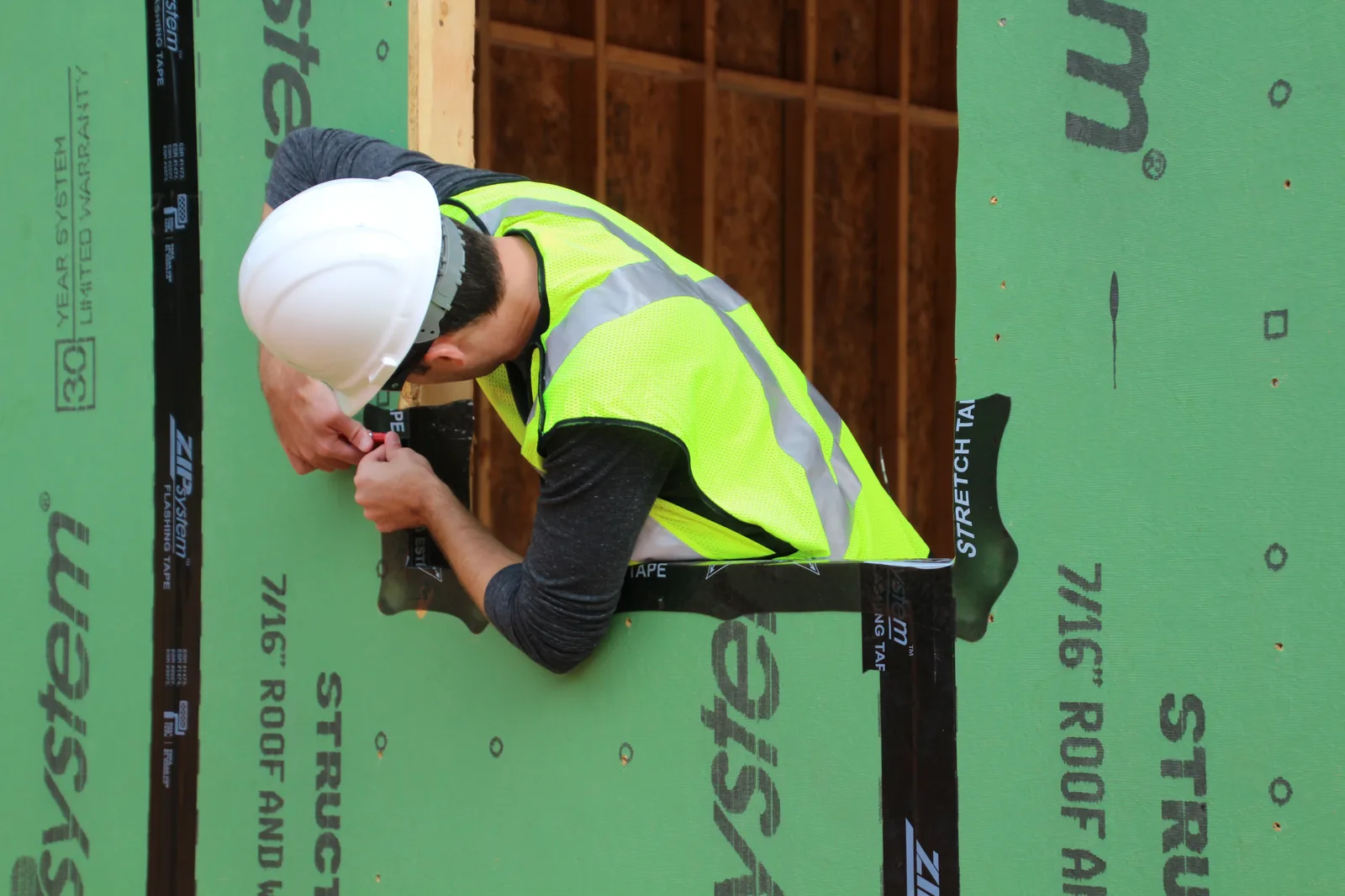 Worker applying flashing tape around a window opening on a sheathed wall